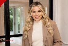 Georgia Kousoulou smiling while wearing a neutral tan blazer and off-white turtleneck sweater inside a modern home.