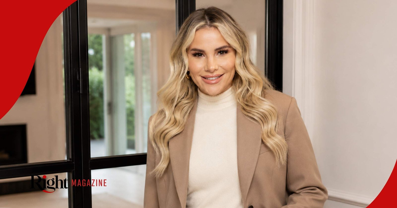Georgia Kousoulou smiling while wearing a neutral tan blazer and off-white turtleneck sweater inside a modern home.