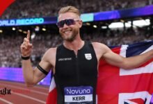 Josh Kerr wearing his black Great Britain kit and running sunglasses, smiling and celebrating on the track while holding the Union Jack flag.