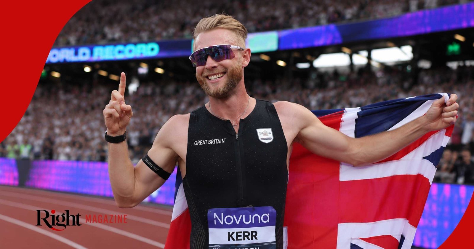 Josh Kerr wearing his black Great Britain kit and running sunglasses, smiling and celebrating on the track while holding the Union Jack flag.