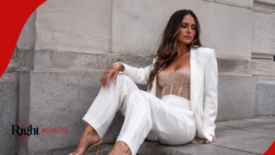 Leah Taylor sitting on a stone step, wearing a chic white pantsuit over a sheer lace bodice, looking away thoughtfully.